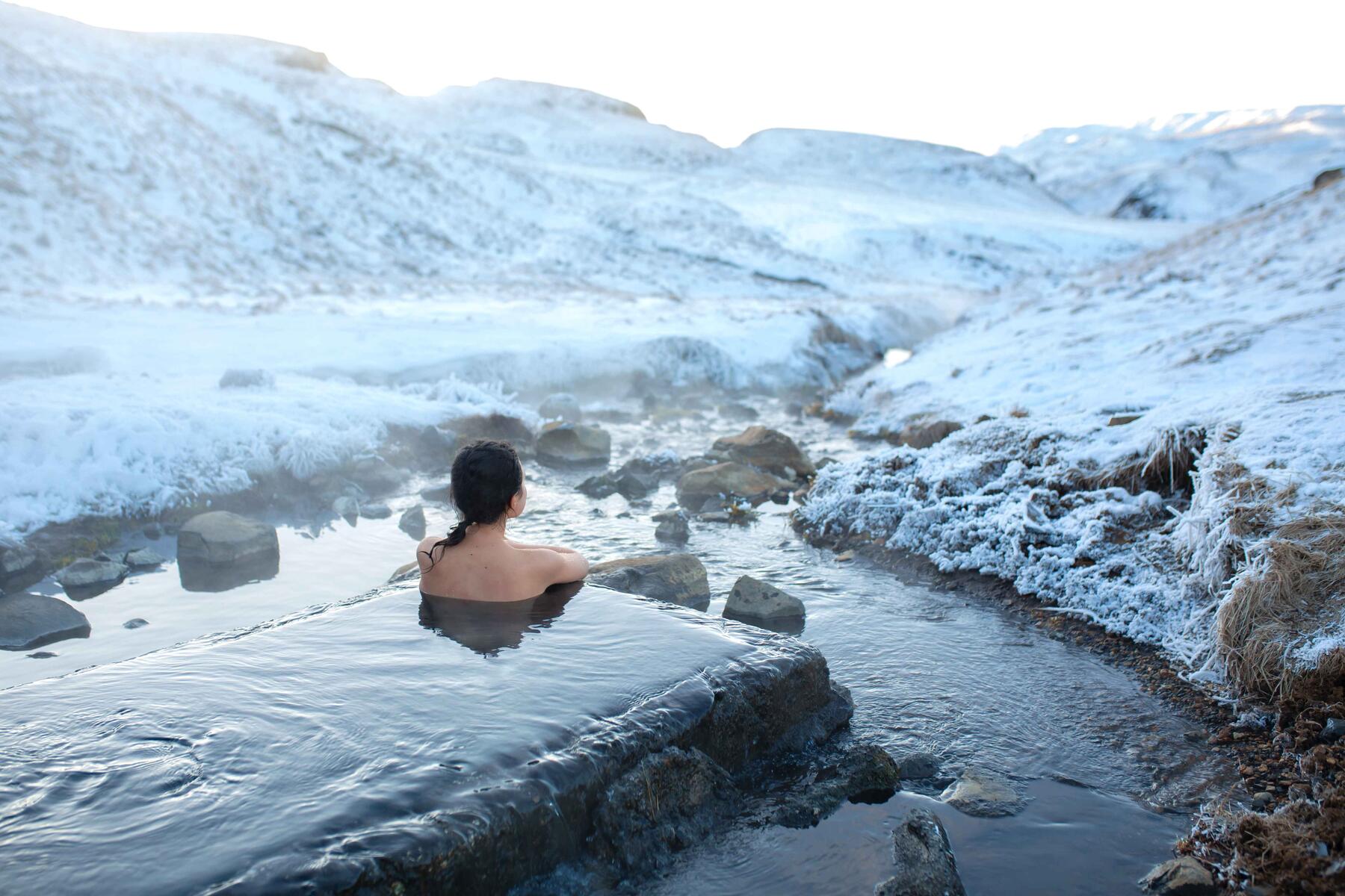 Person soaking in a steaming river surrounded by snowy hills in Iceland